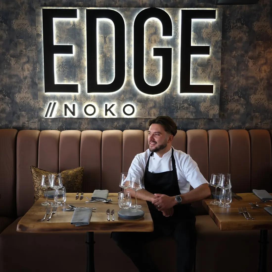 Alex Clare seated in front of the Edge//Noko sign
