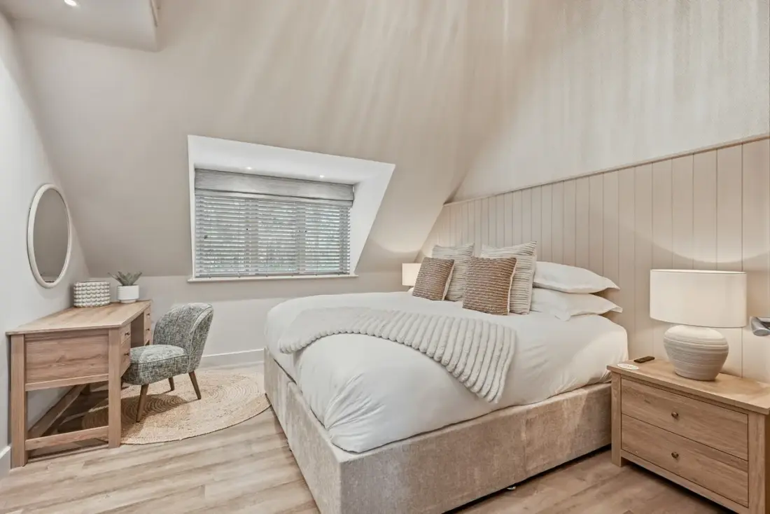 A bedroom with a sloping ceiling, a large bed and a small window